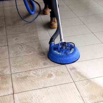 A person using a blue floor cleaning machine on tiled floor; the tiles are being cleaned.