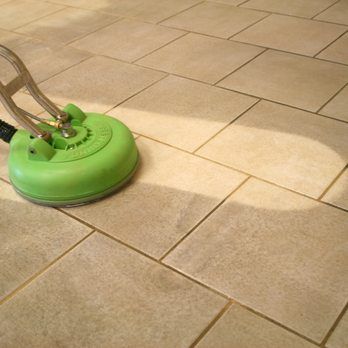 Green floor cleaner scrubbing beige tile floor.