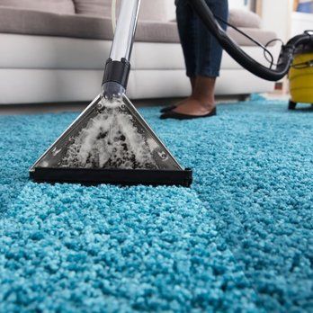 Person vacuuming a teal carpet with a carpet cleaner in a living room.