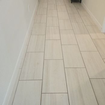 Light-colored rectangular tiles cover a hallway floor; white wall and baseboard on the left.
