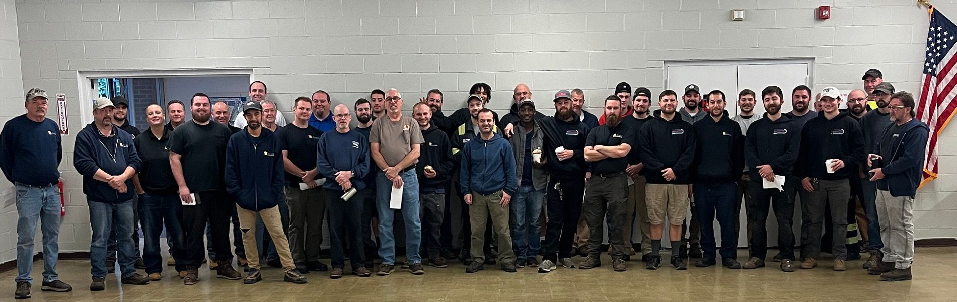 Group of men standing in a room with an American flag. They are wearing various dark clothing.