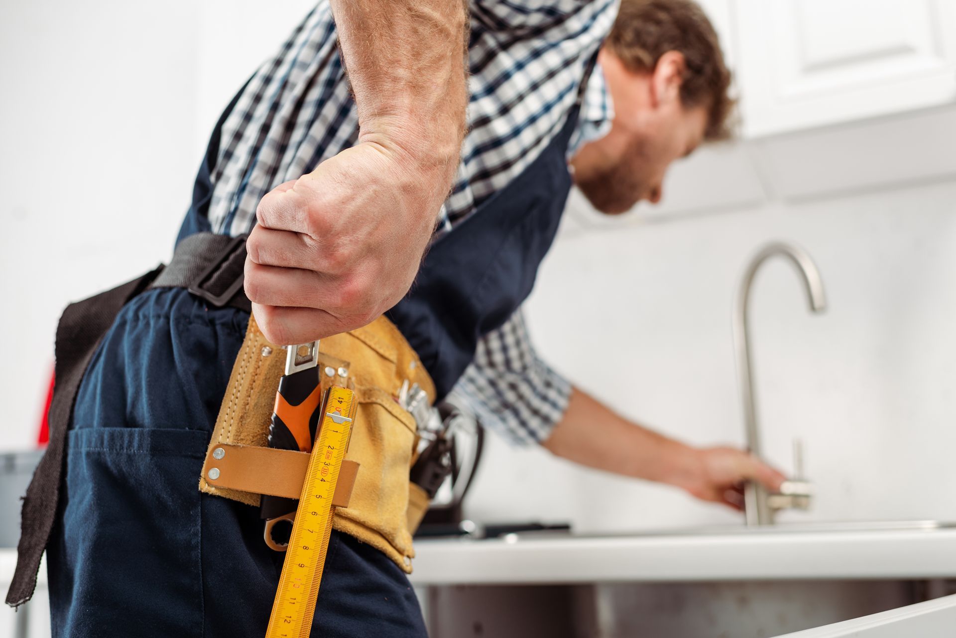 Plumber in work overalls and tool belt repairing a kitchen sink faucet in a residential home