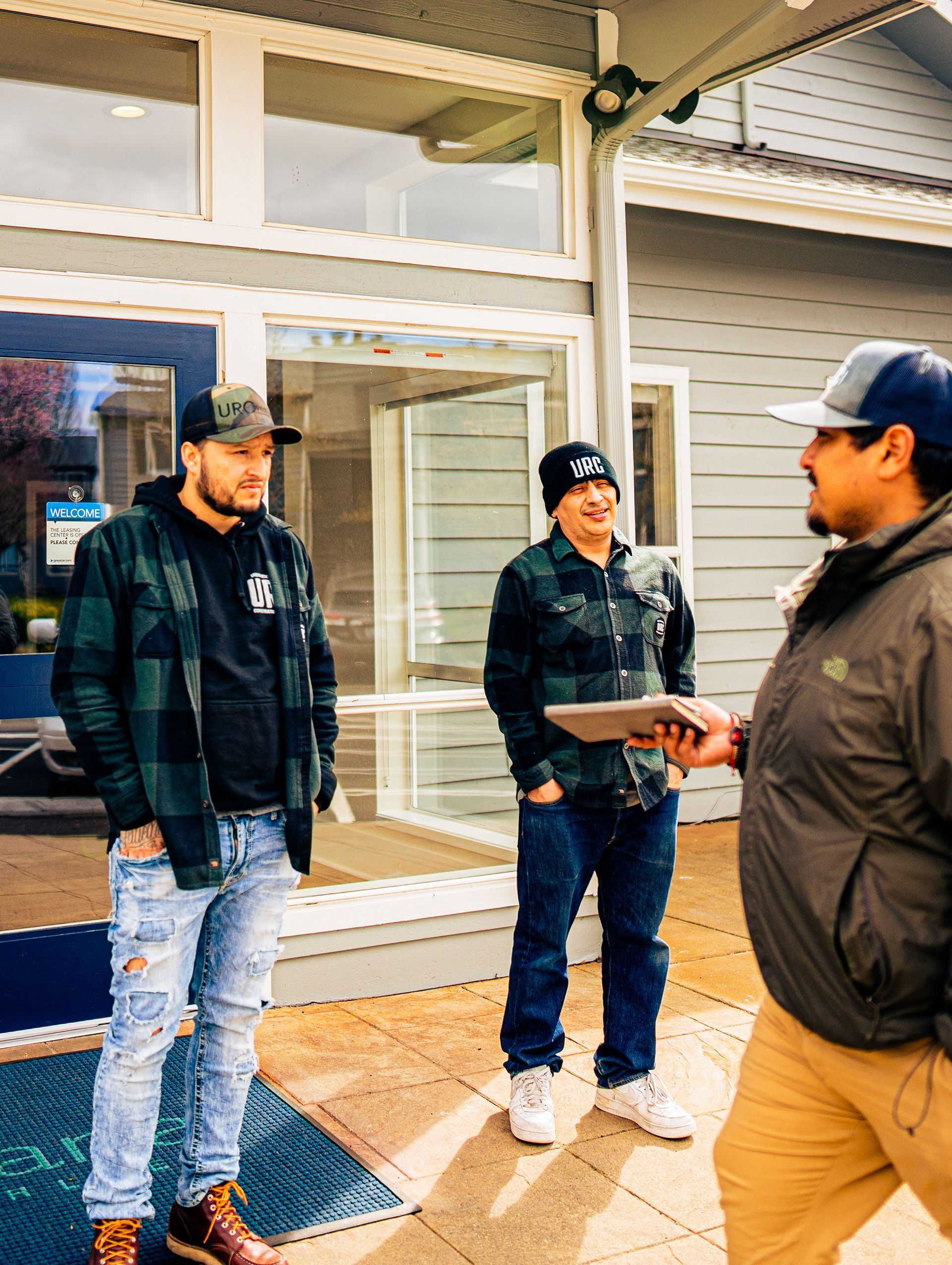 Three men are standing in front of a building talking to each other.