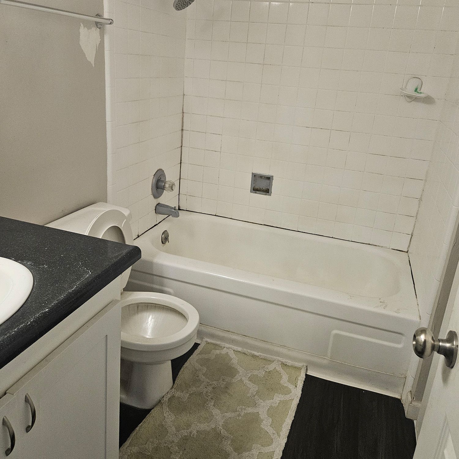 Bathroom with white tile, tub, toilet, vanity, and a green rug.