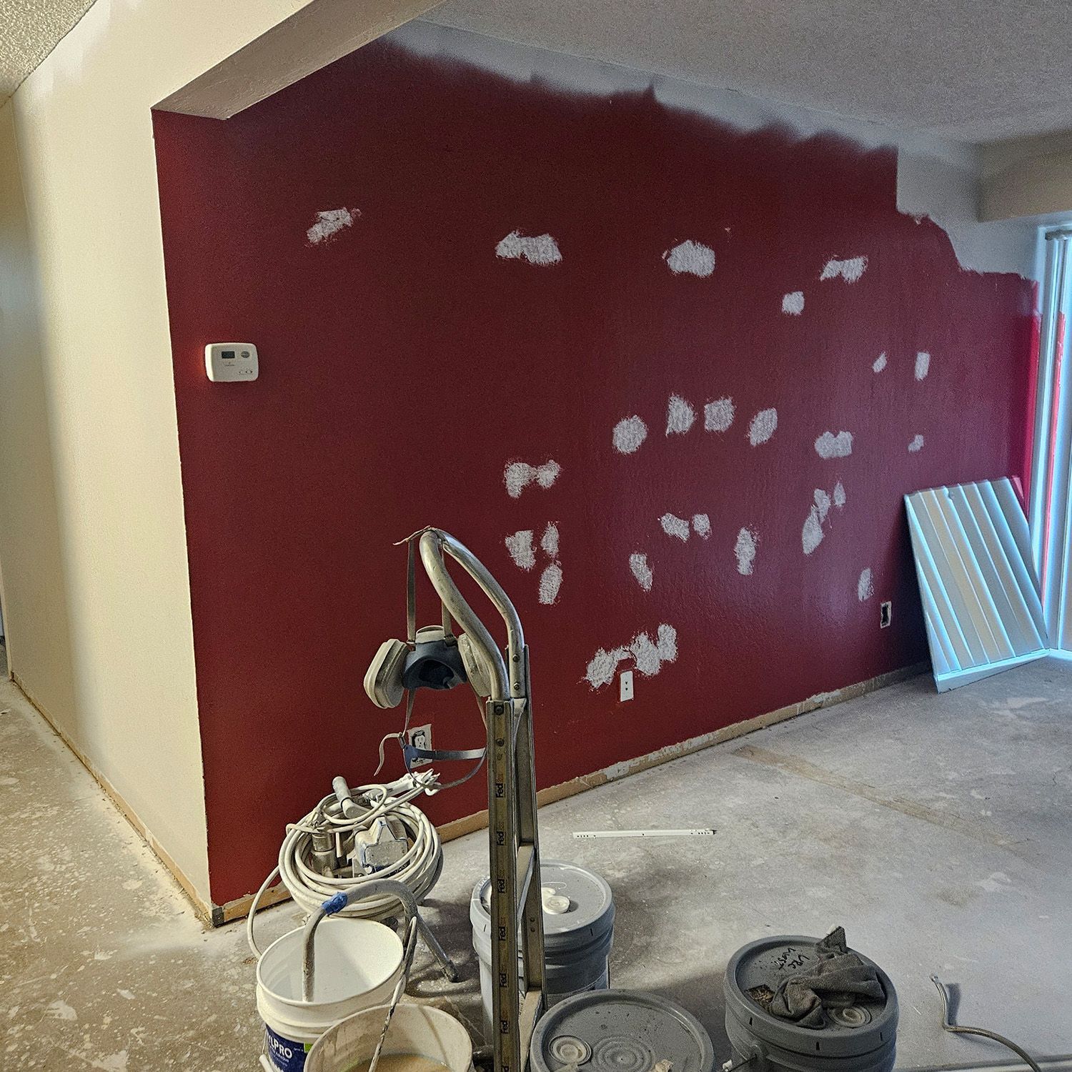 Room with red wall being patched, painting equipment visible.