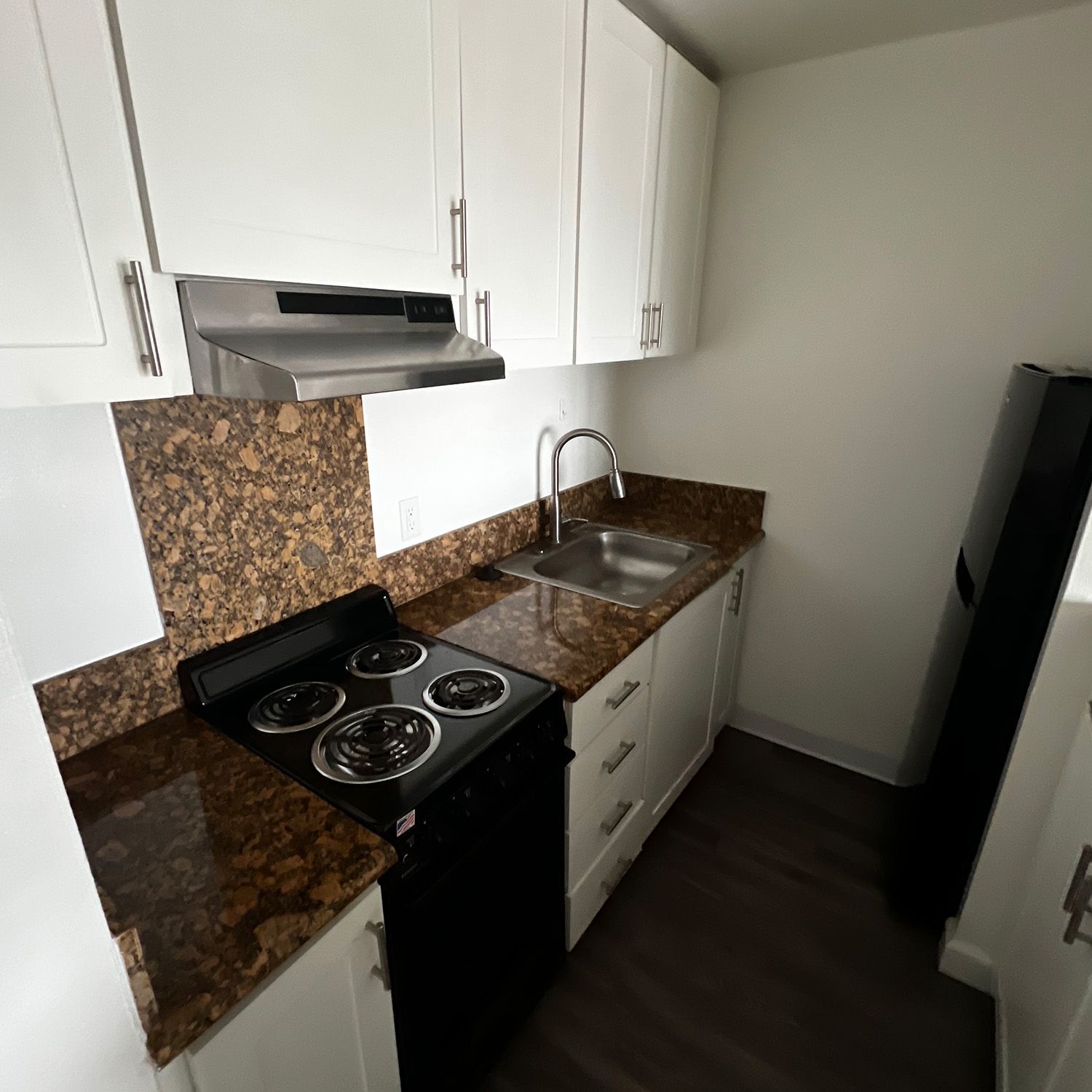 Small kitchen with white cabinets, brown countertop, black stove and a stainless steel sink.