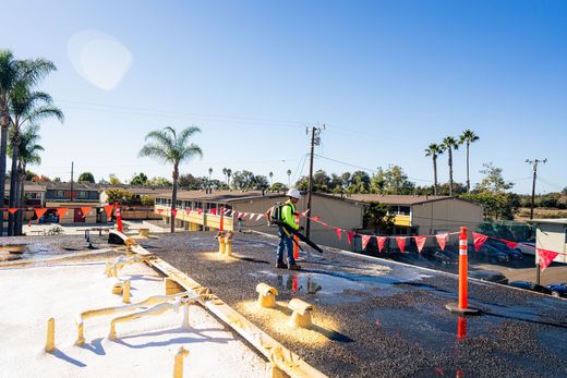 Road construction site with workers, orange safety cones, and wet asphalt under a clear blue sky