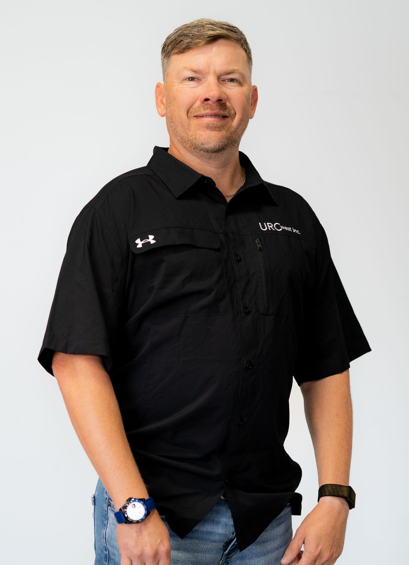 Man standing against a plain background, wearing a black button-up shirt and jeans.