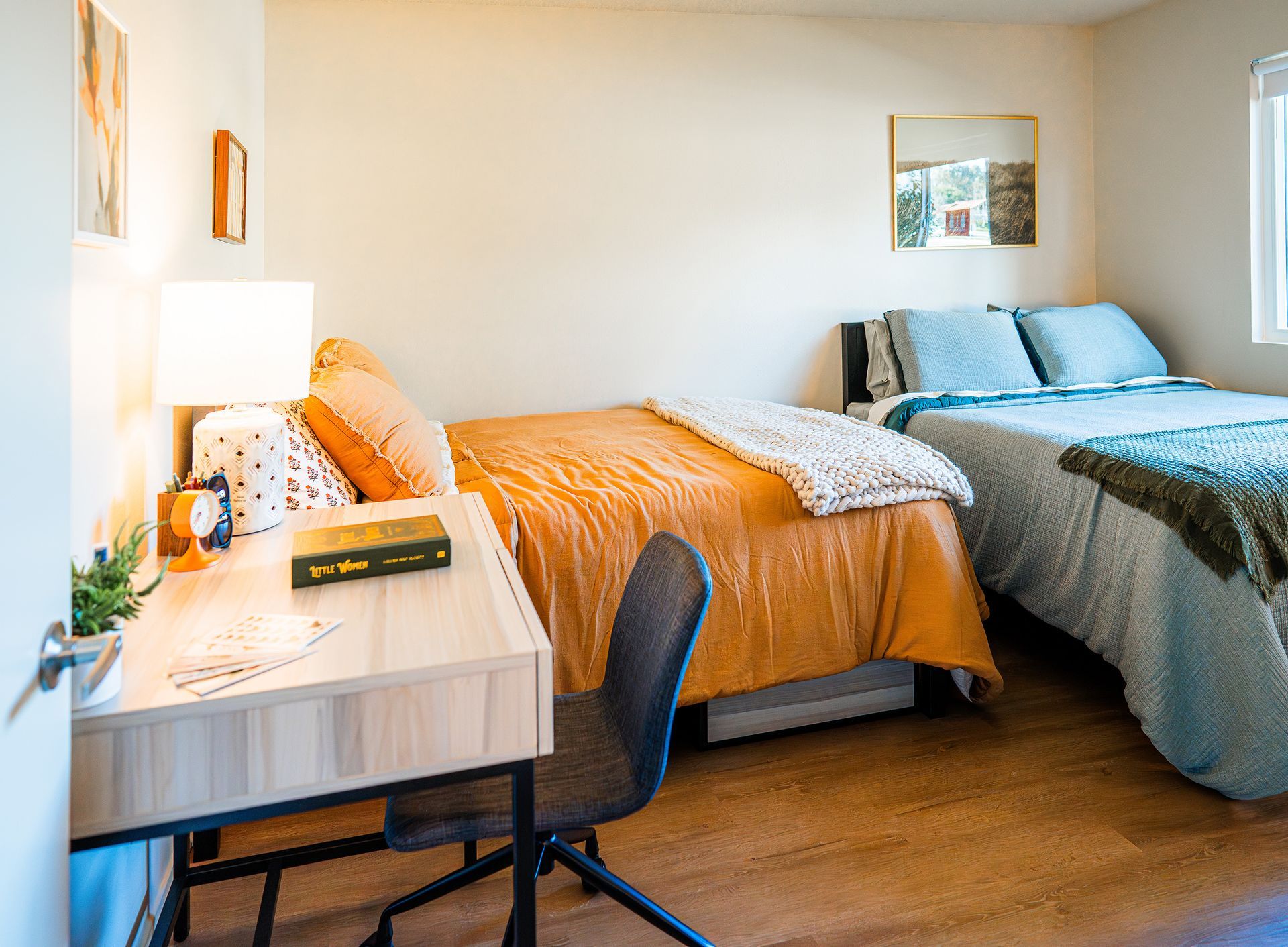 Small bedroom with two beds, desk, lamp, and bright orange and gray bedding