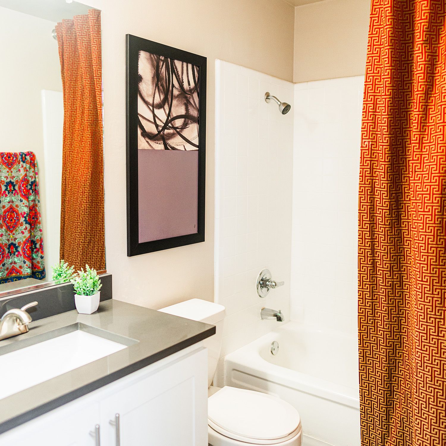 Bathroom with orange patterned shower curtain, white bathtub, and sink. Artwork on wall.