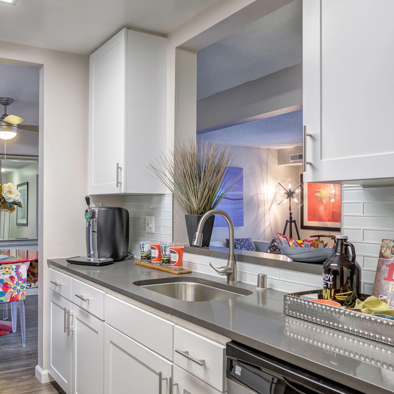 White kitchen with gray countertops, stainless steel sink, and open view to living area.