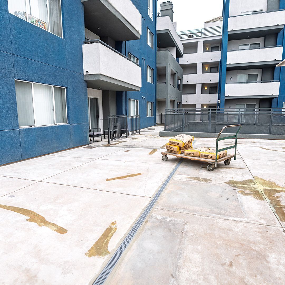 Blue apartment building exterior with a hand truck holding construction materials on a concrete patio.