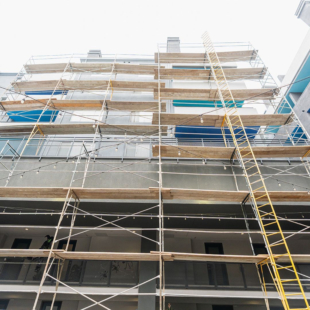 Scaffolding on an apartment building for repairs, with wooden planks and yellow ladder.