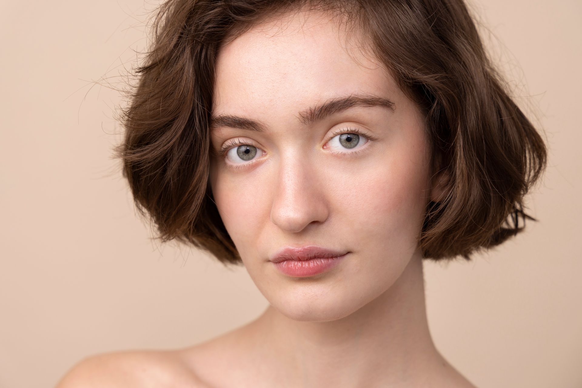 A close up of a woman 's face with short hair on a beige background.