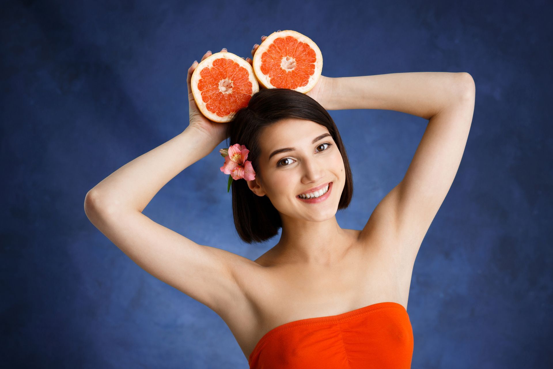 A woman in a red dress is holding grapefruit slices on her head.