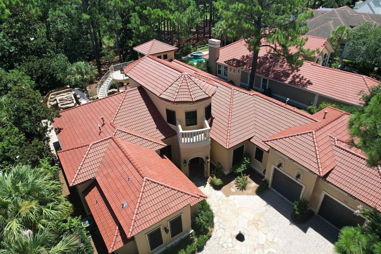 Aerial view of a Spanish-style house with red tile roof, surrounded by trees, and a stone driveway.