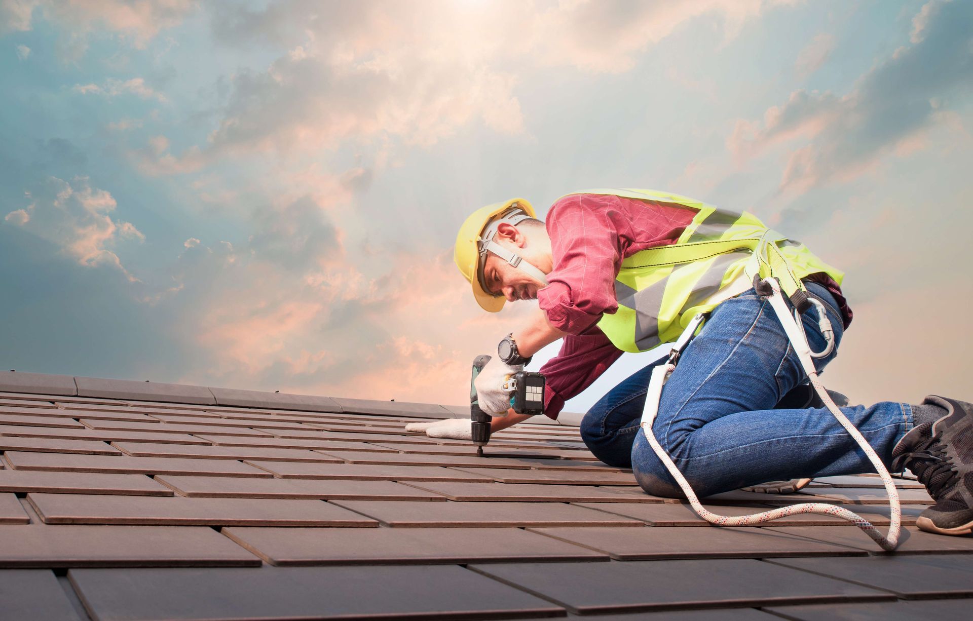 A dedicated roofing contractor using a power drill to secure tiles on a residential roof project.