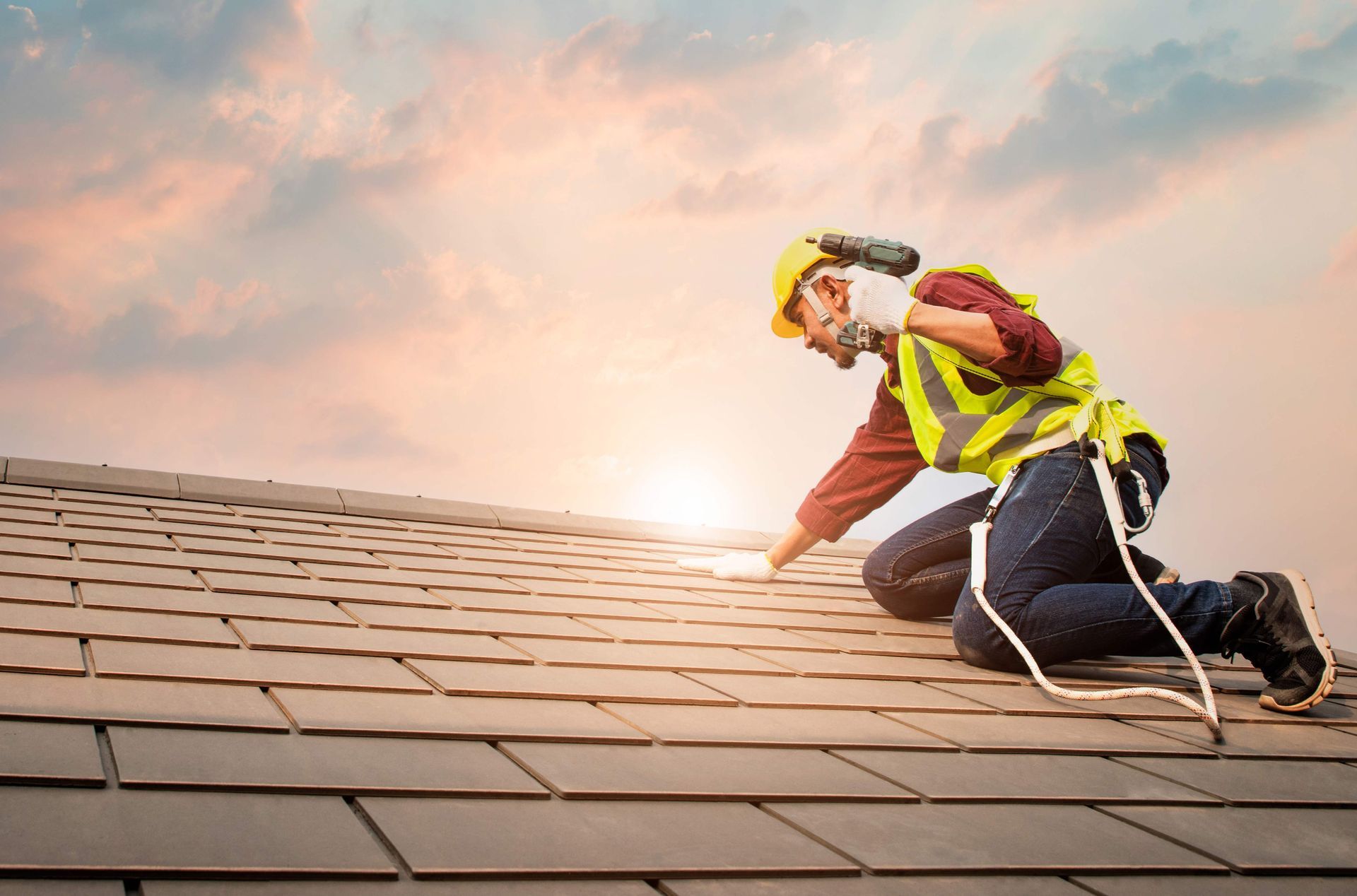 A professional roofing contractor wearing safety gear while inspecting a shingle roof at sunset.