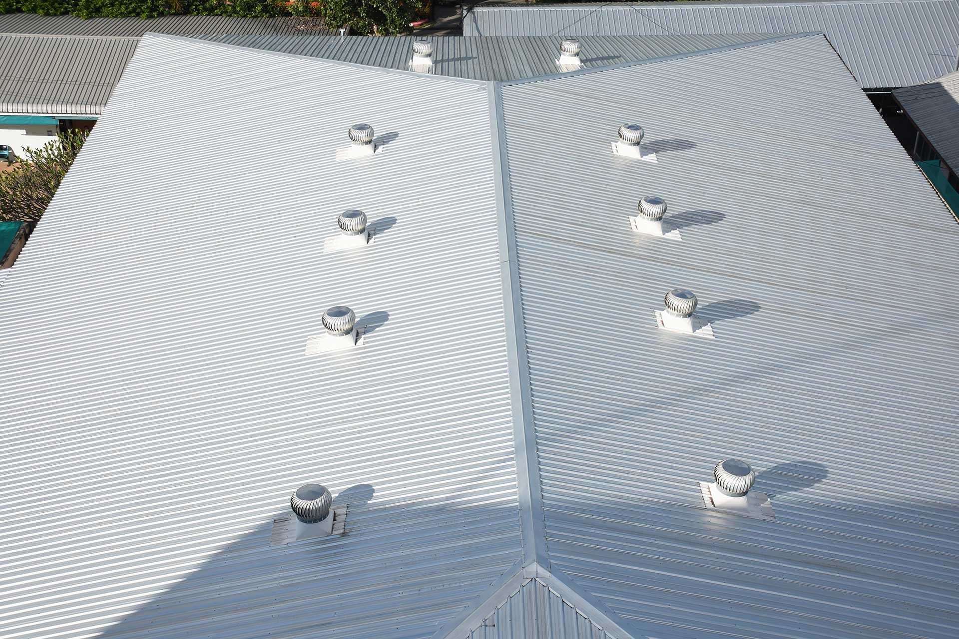 High-angle view of a corrugated metal roof with multiple white vents, reflecting sunlight.