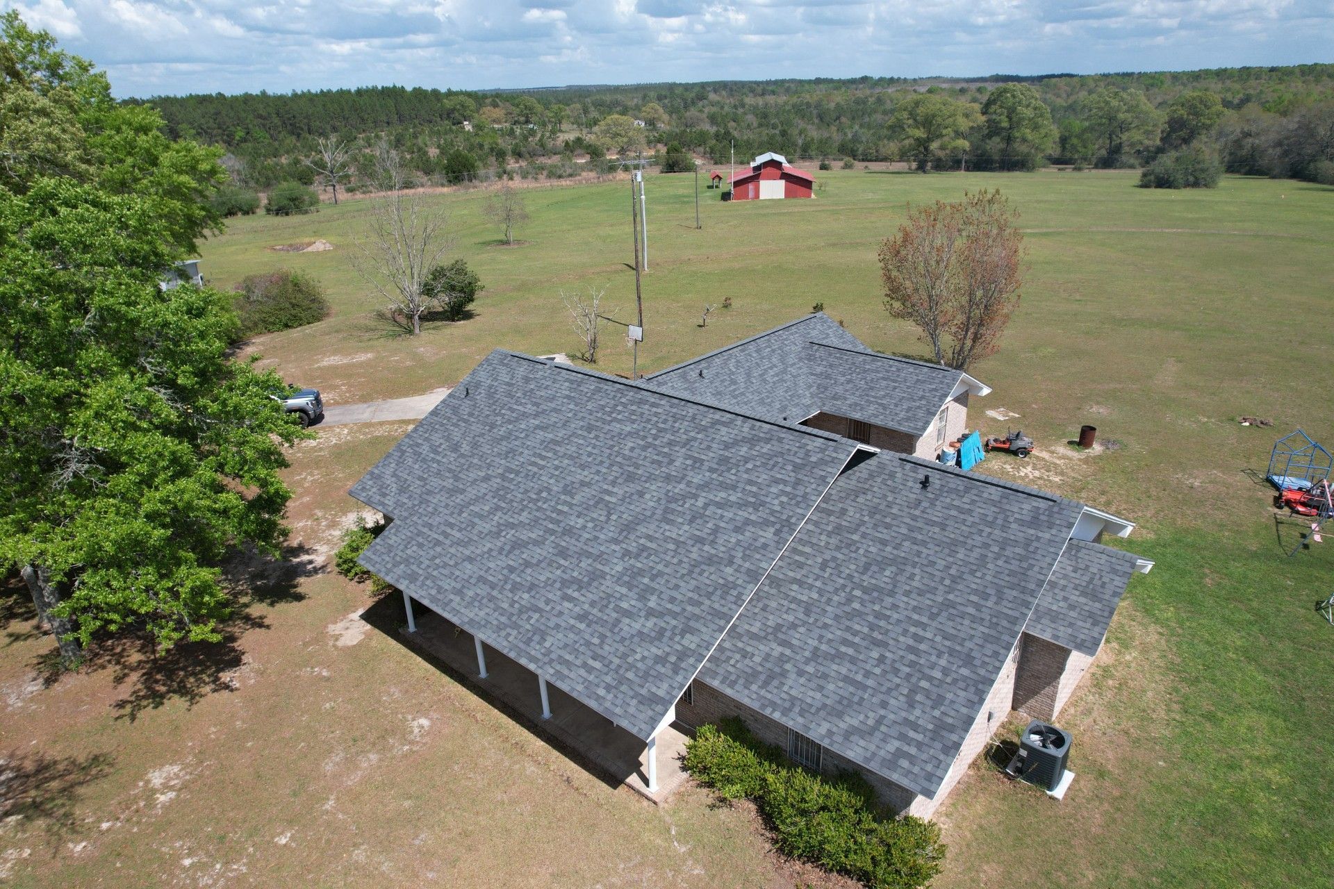 Aerial view of a gray-roofed house with a large yard and fields around it