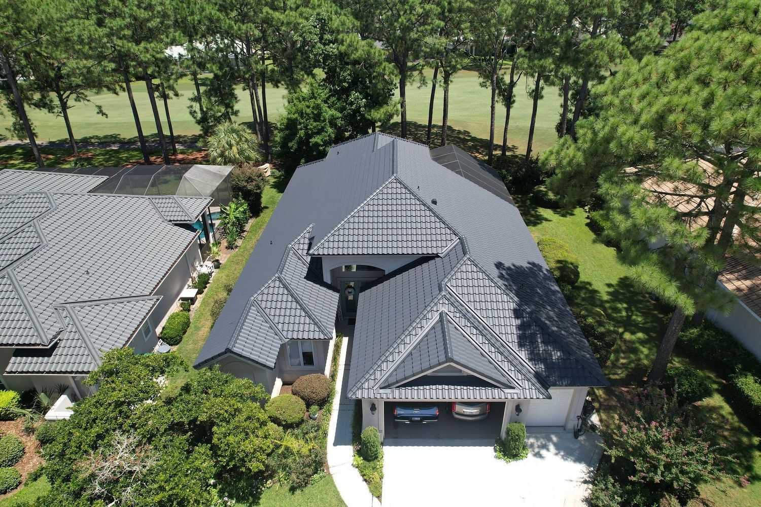 Aerial view of a modern house with a dark gray tiled roof, a two-car garage, and lush green surroundings.