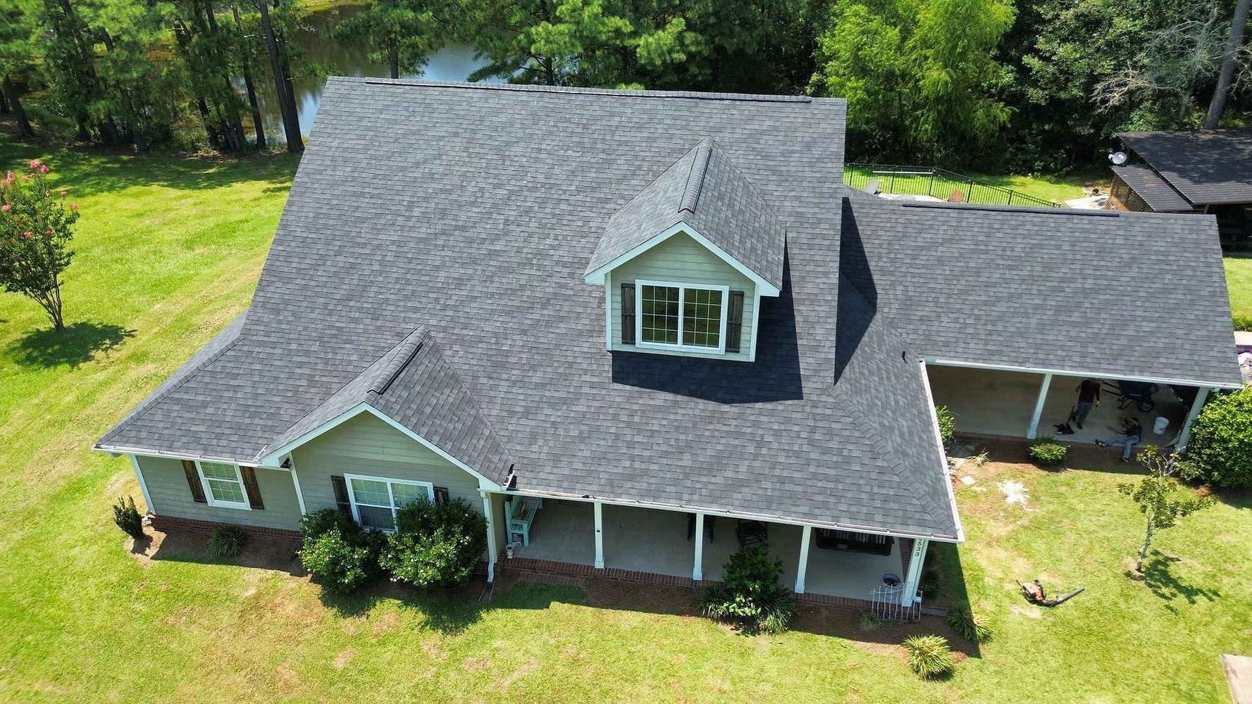 A house with a gray roof and light green siding, a porch, and a small dormer window.
