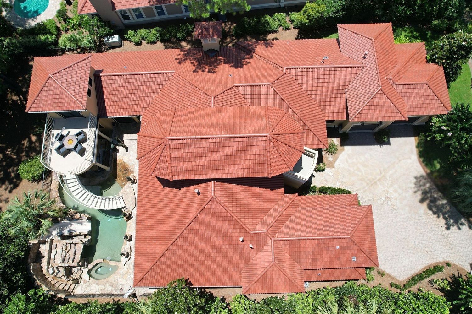 Aerial view of a large house with a red tile roof, pool, and patio.