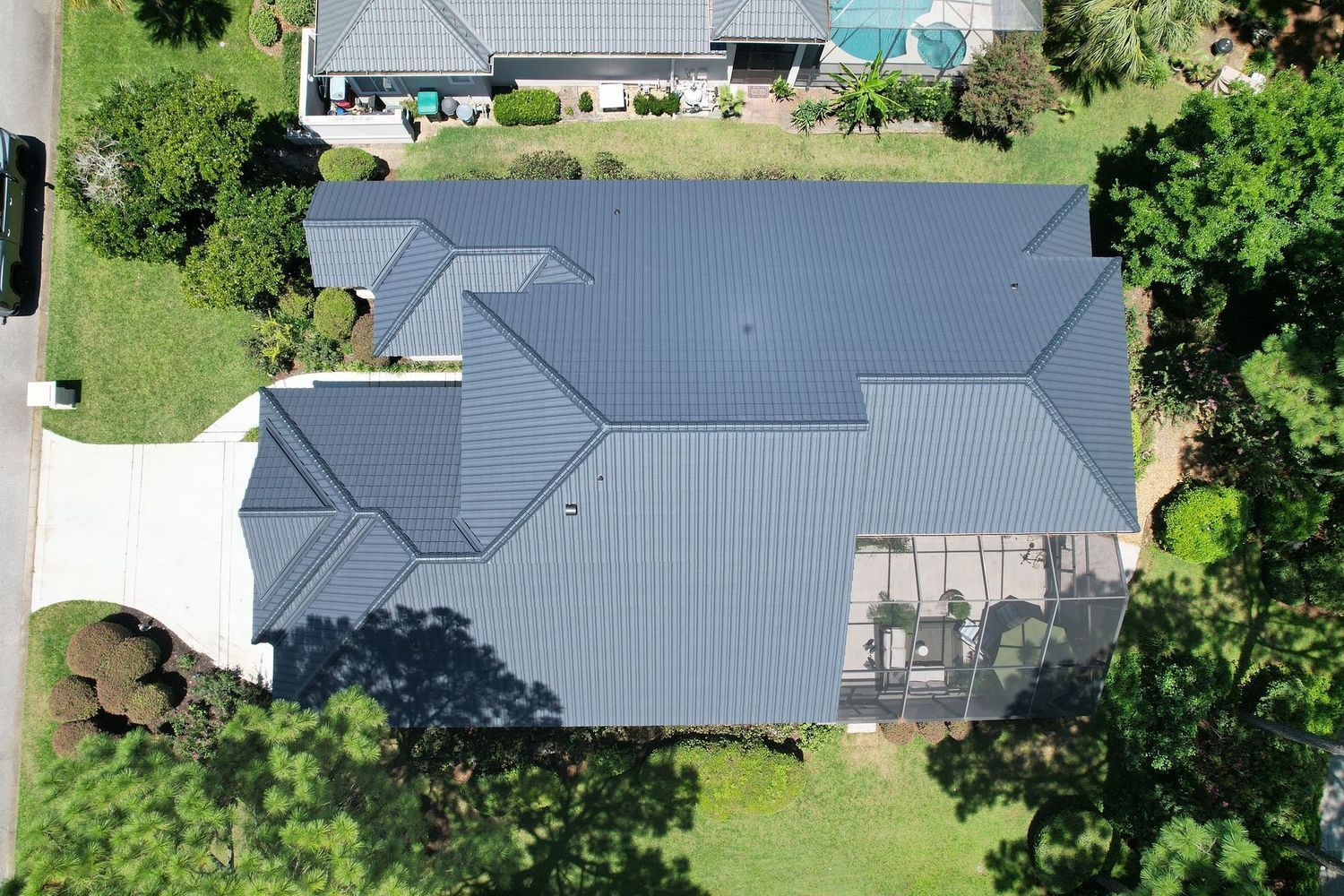 Aerial view of a house with a dark gray roof surrounded by trees and a driveway.