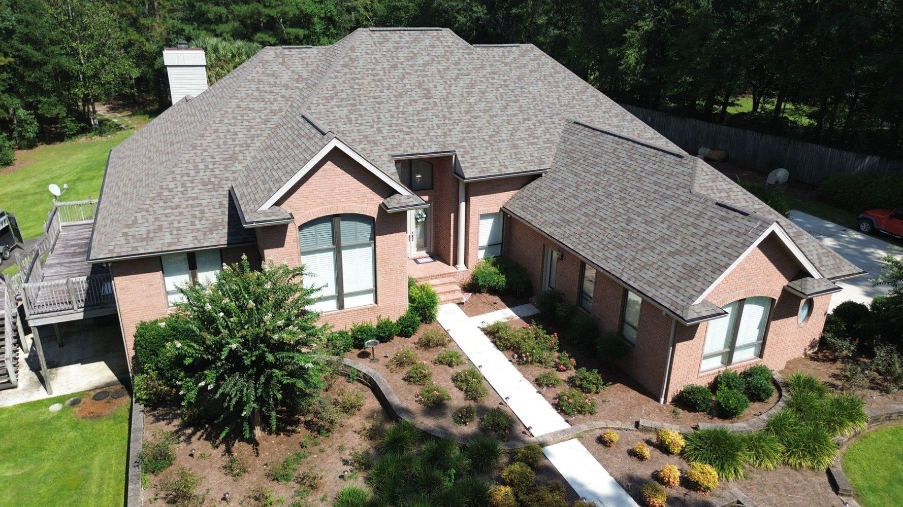 Brick house with brown roof, front landscaping, and a side deck.