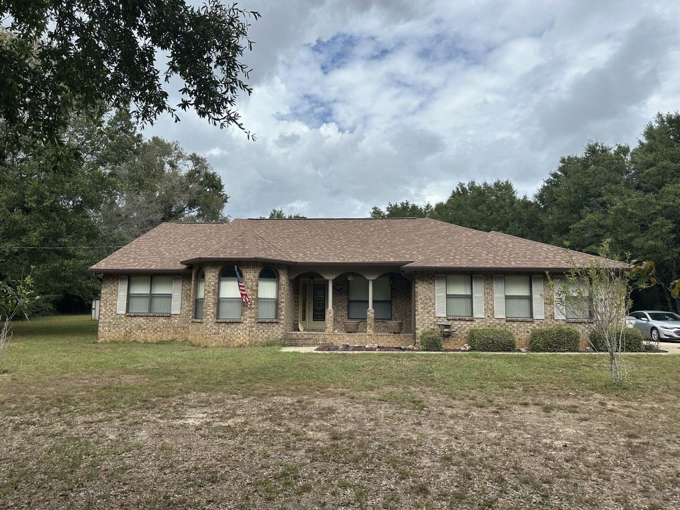 Ranch-style house with stone facade, brown roof, and green lawn under a cloudy sky.