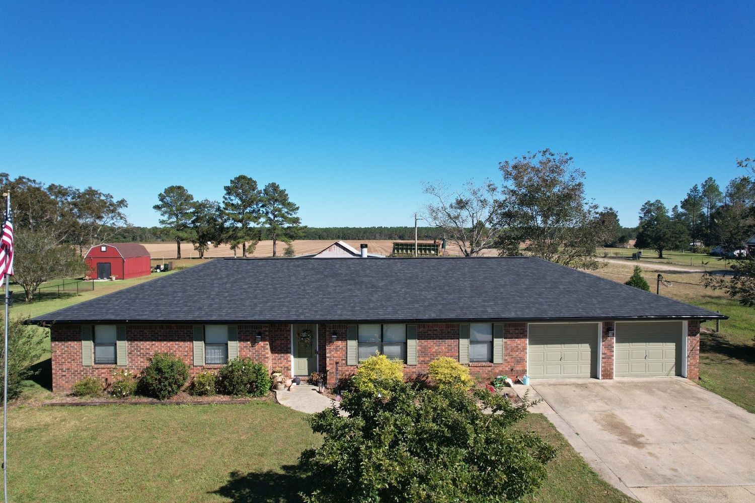 Brick house with a dark gray roof, two-car garage, and American flag on a sunny day.