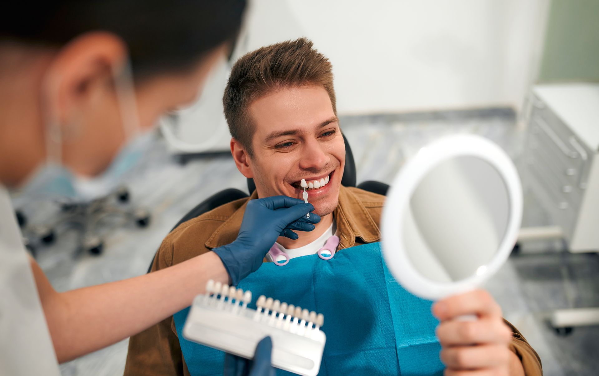 Dentist using dental tools to perform teeth whitening on a smiling patient in bright clinic.
