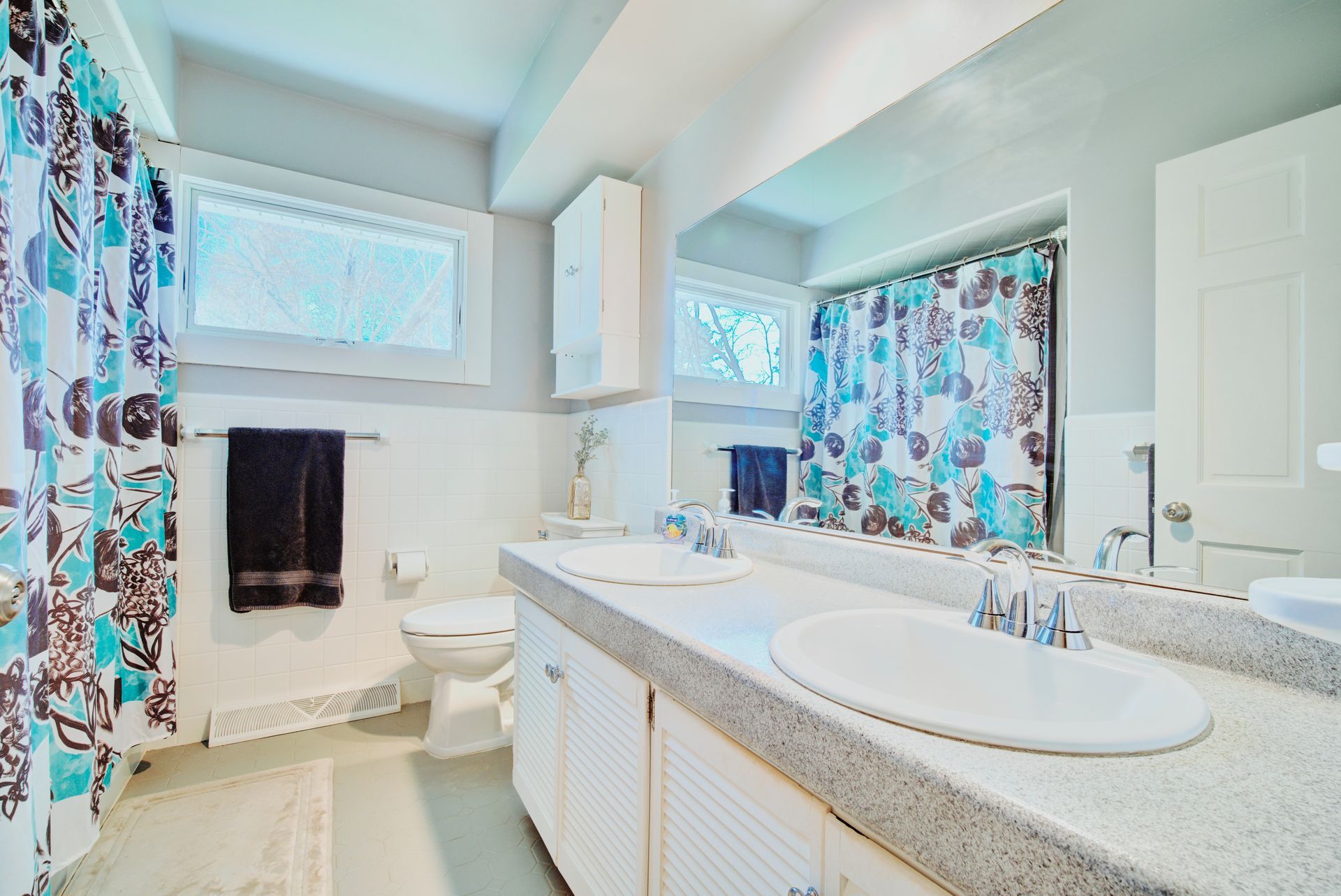 Bathroom with double sinks, floral shower curtain, and window.