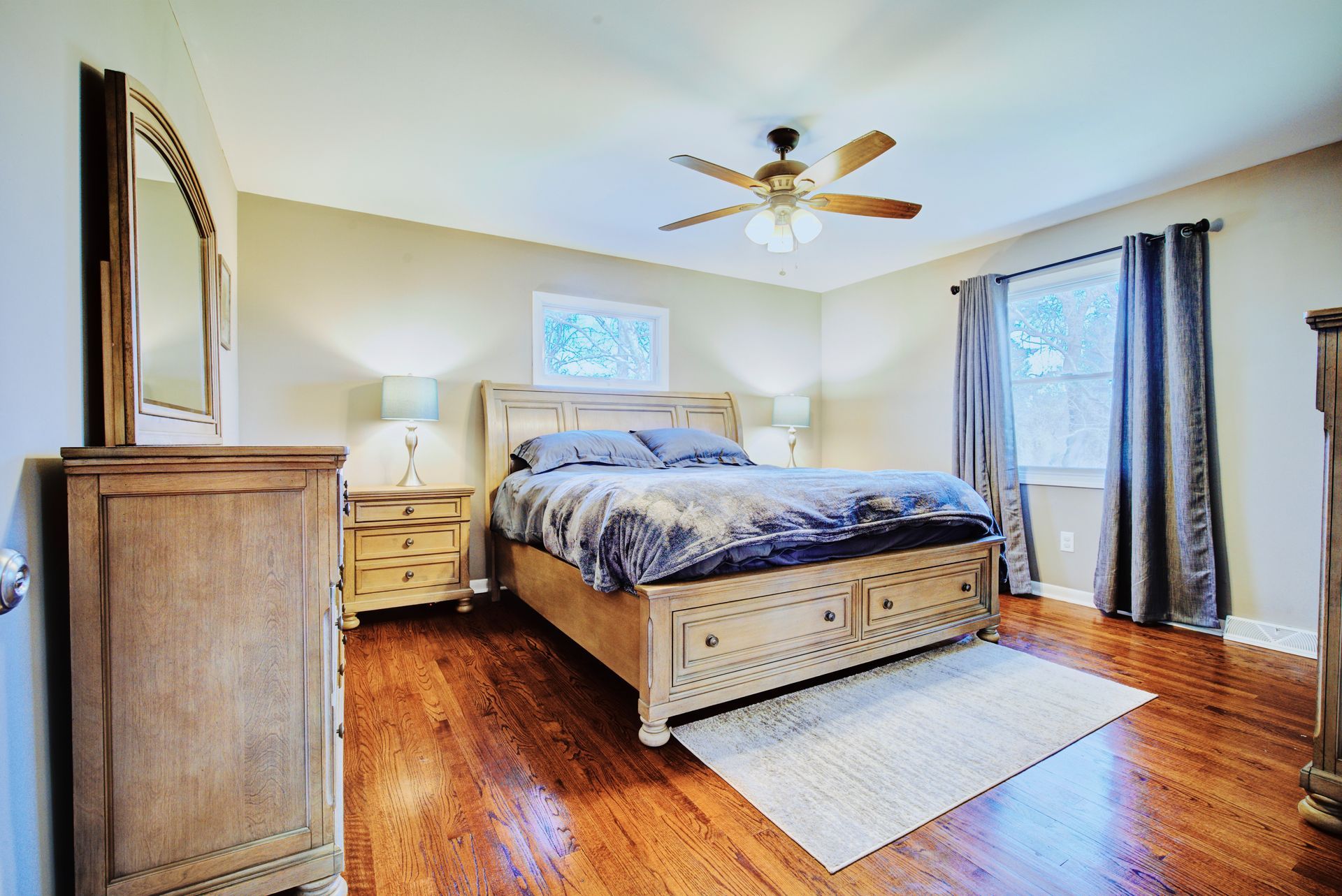 Bedroom with a wooden bed, dresser, and hardwood floors. Beige walls and gray curtains.