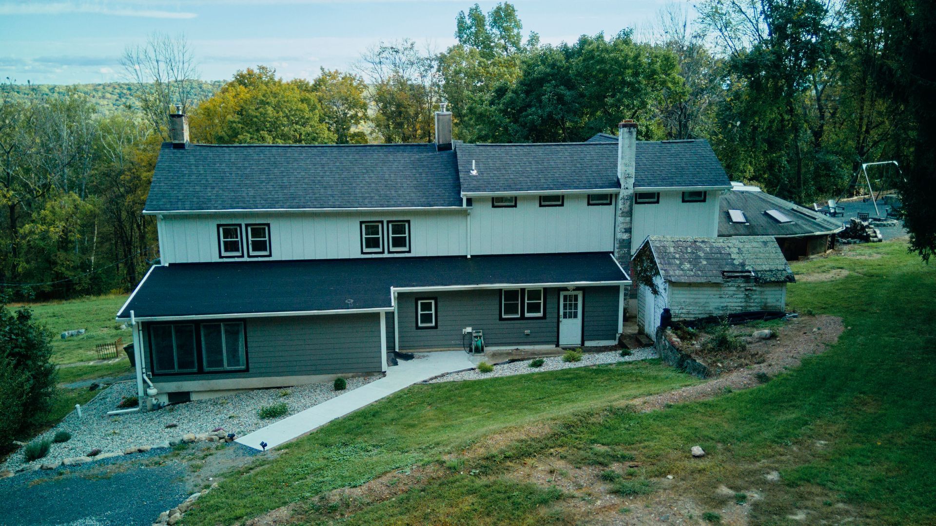 A large house with a black roof is sitting on top of a lush green hillside.