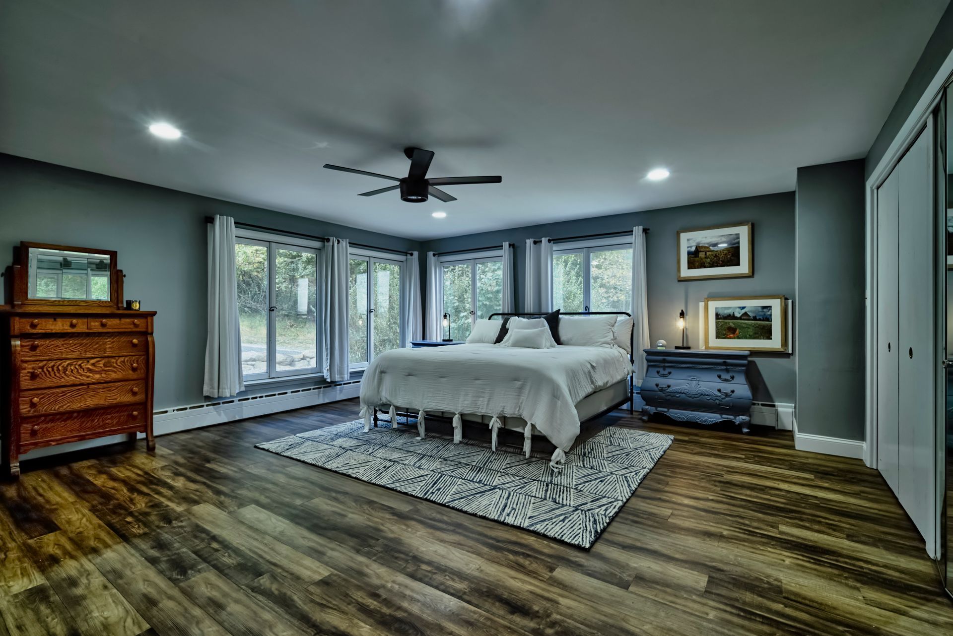 A bedroom with hardwood floors , a large bed , a dresser , and a ceiling fan.