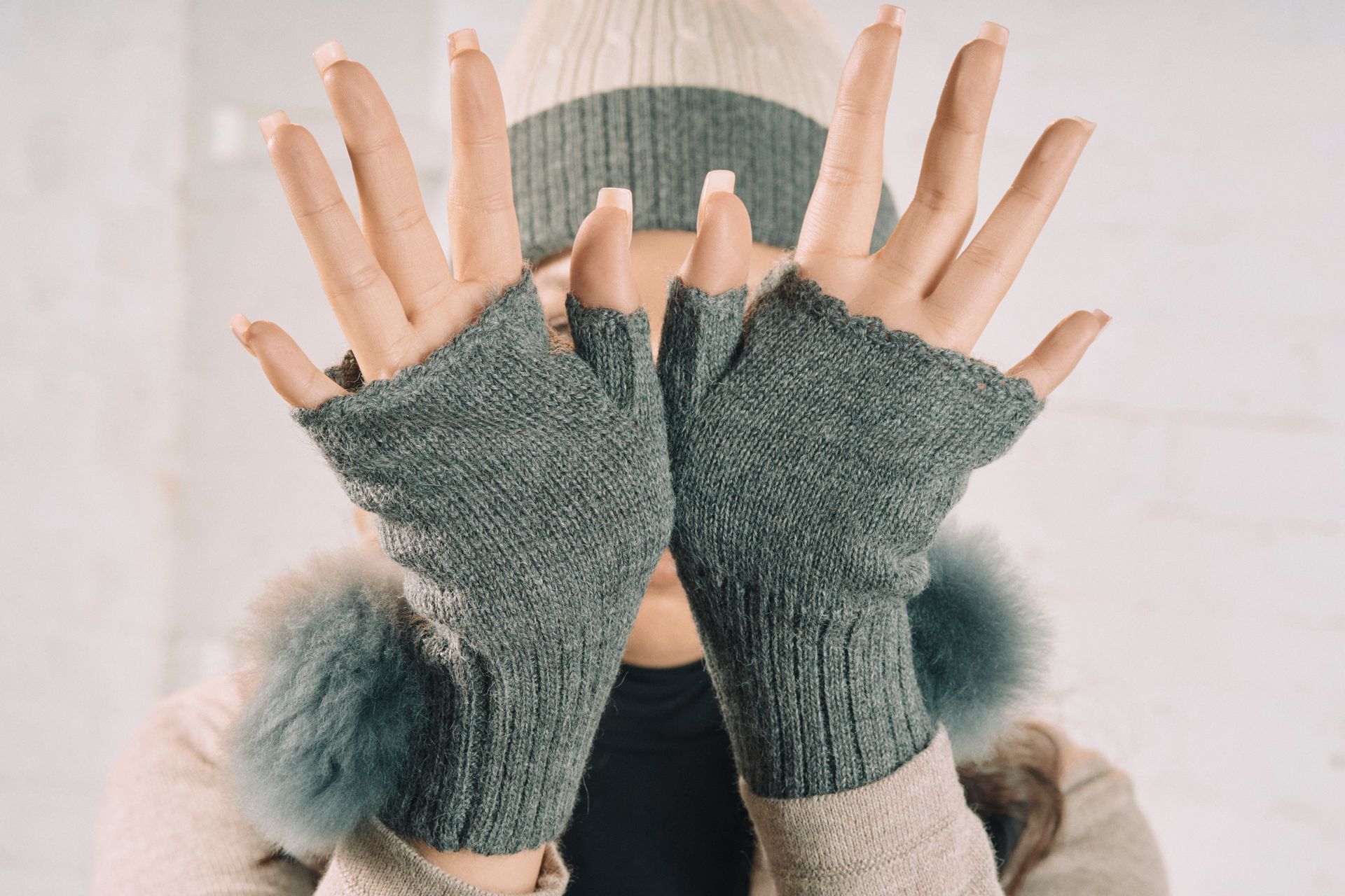 Person wearing grey fingerless gloves, beanie, and headband, hands in front of face.