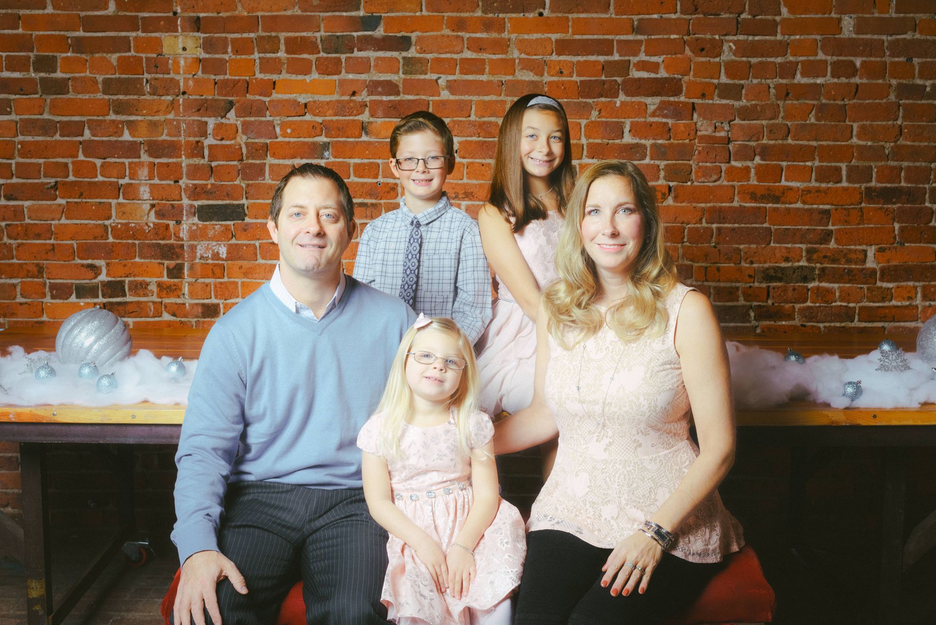 Family of five poses for a photo in front of a brick wall; smiles, holiday theme.