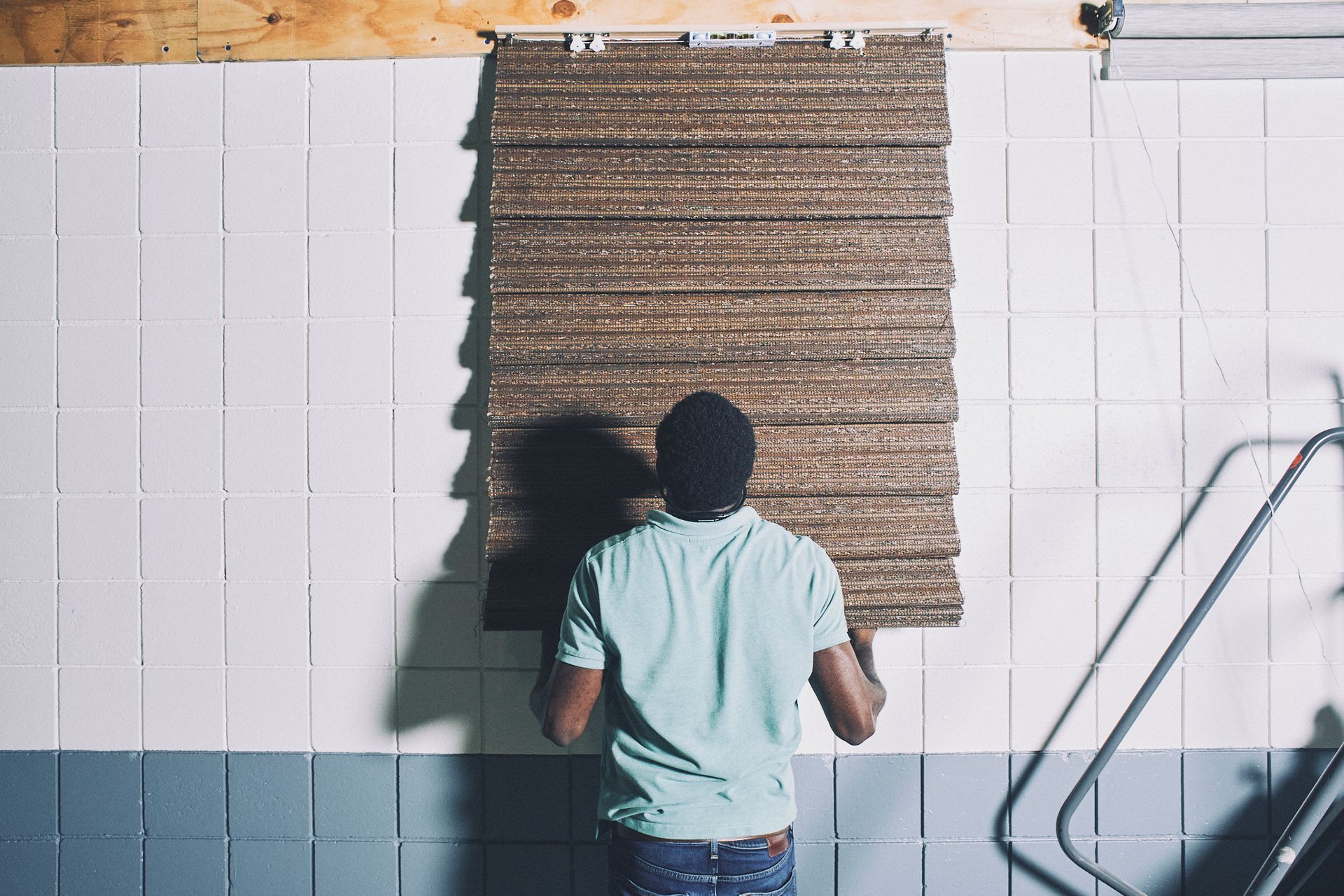 A man is standing in front of a brick wall holding a piece of wood.