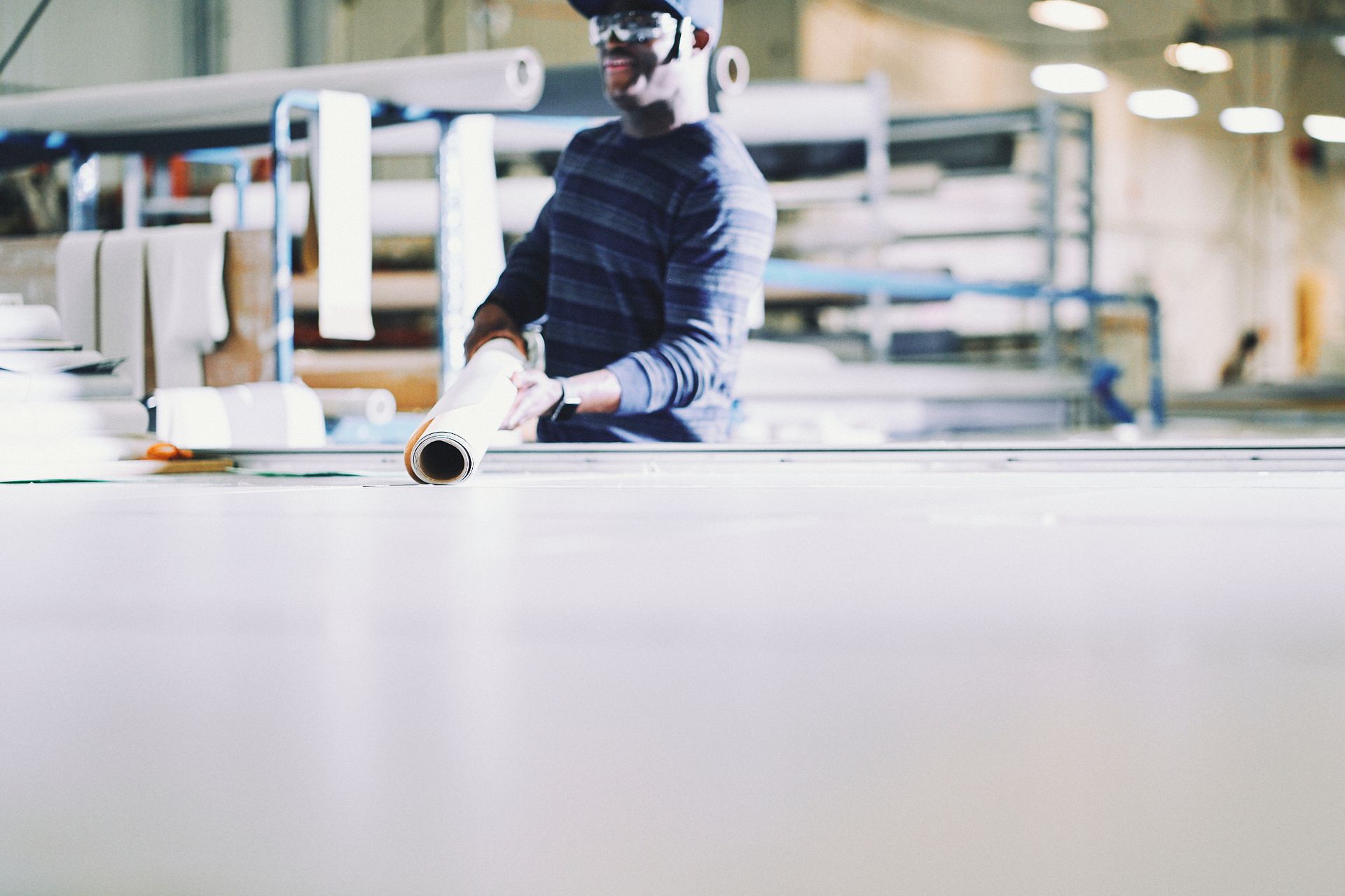 A man is standing in a factory holding a roll of paper.