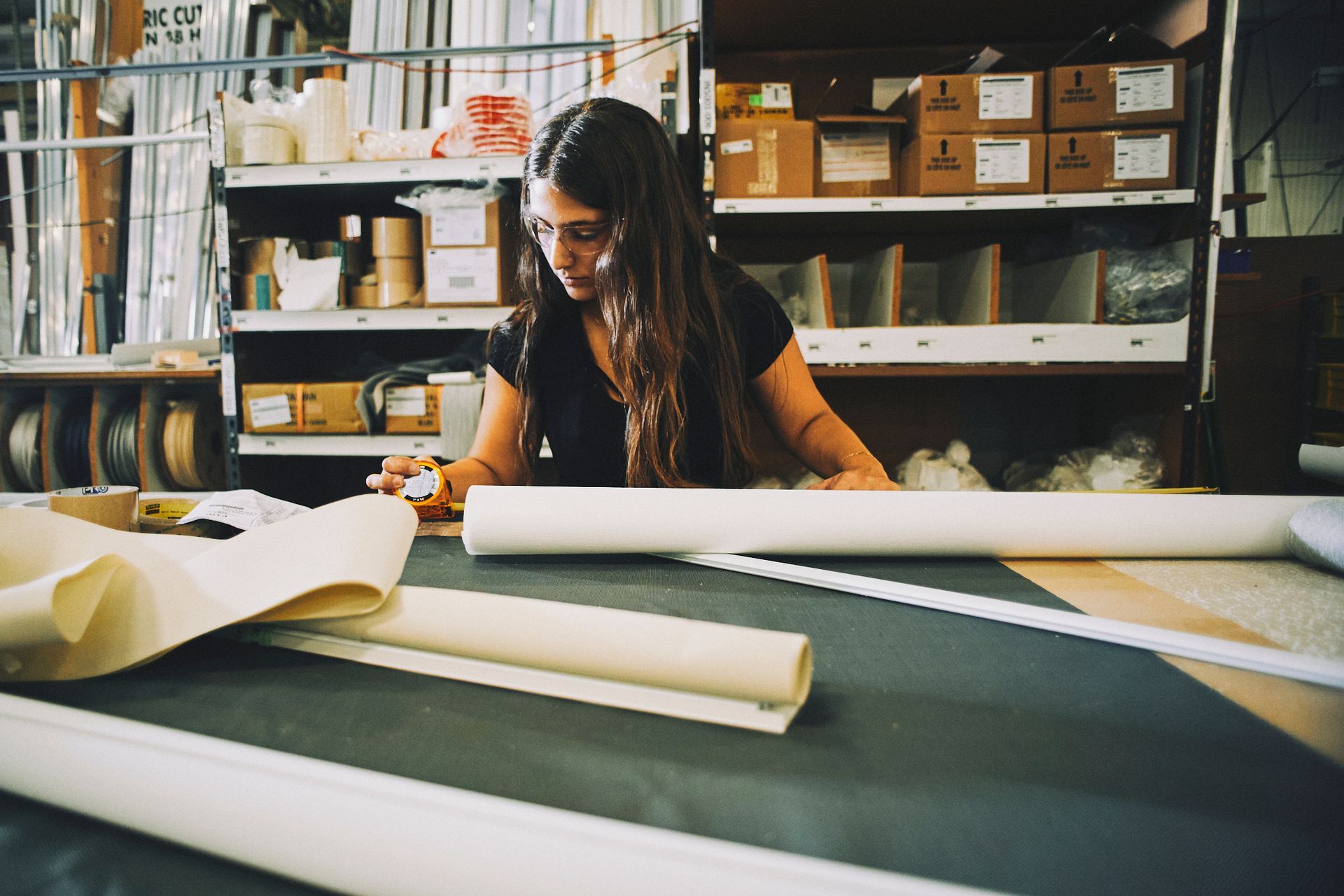 A woman is sitting at a table in a factory working on a piece of paper.