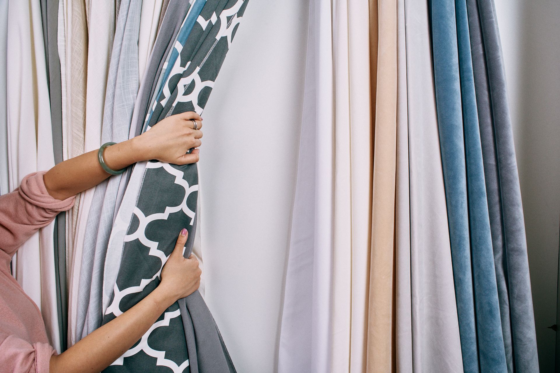 A woman is holding a curtain in front of a wall of curtains.