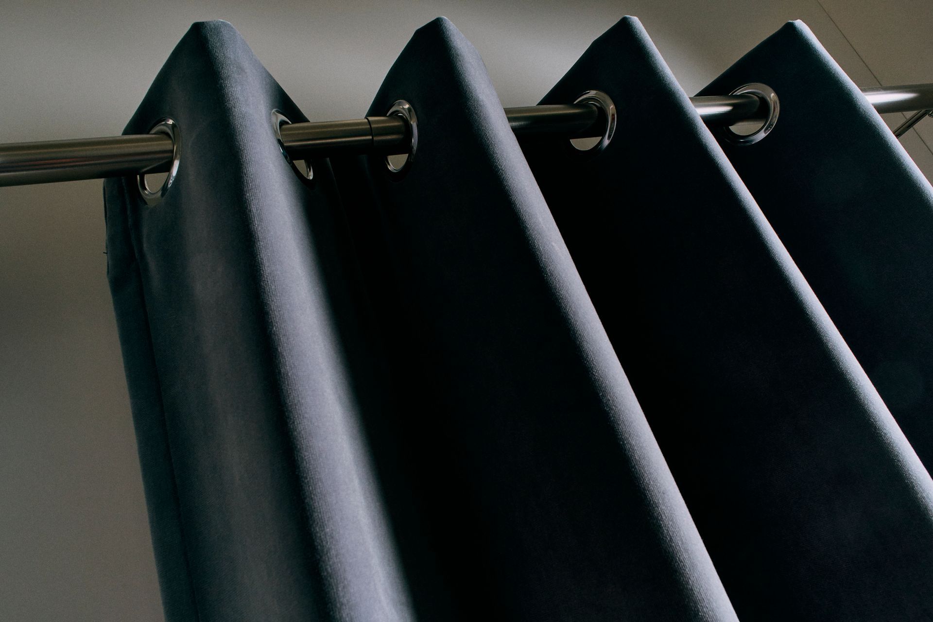 Dark blue curtains with silver grommets hanging from a silver rod.