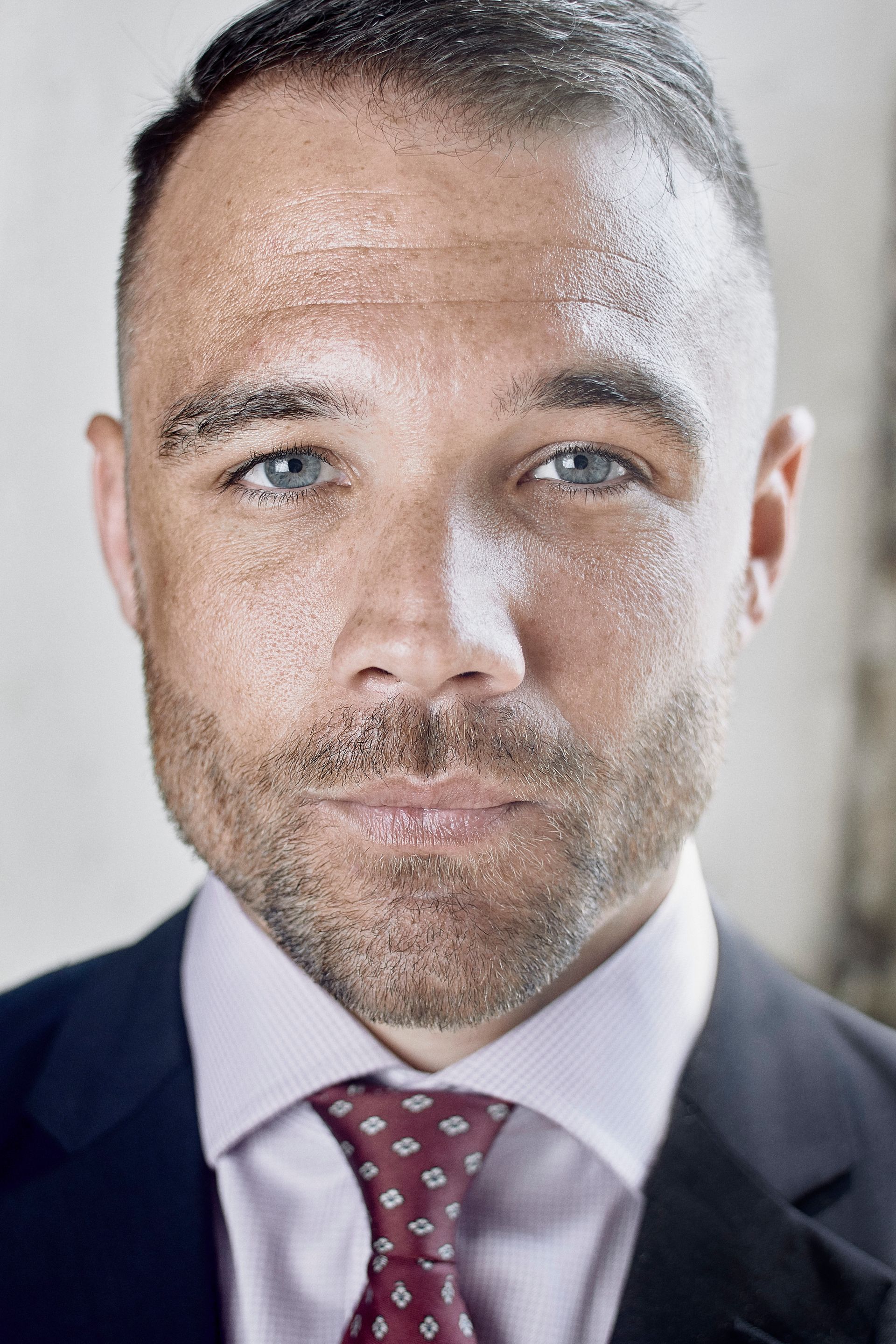 A man with short hair in a suit looks at the camera. His skin is covered in sparkle.