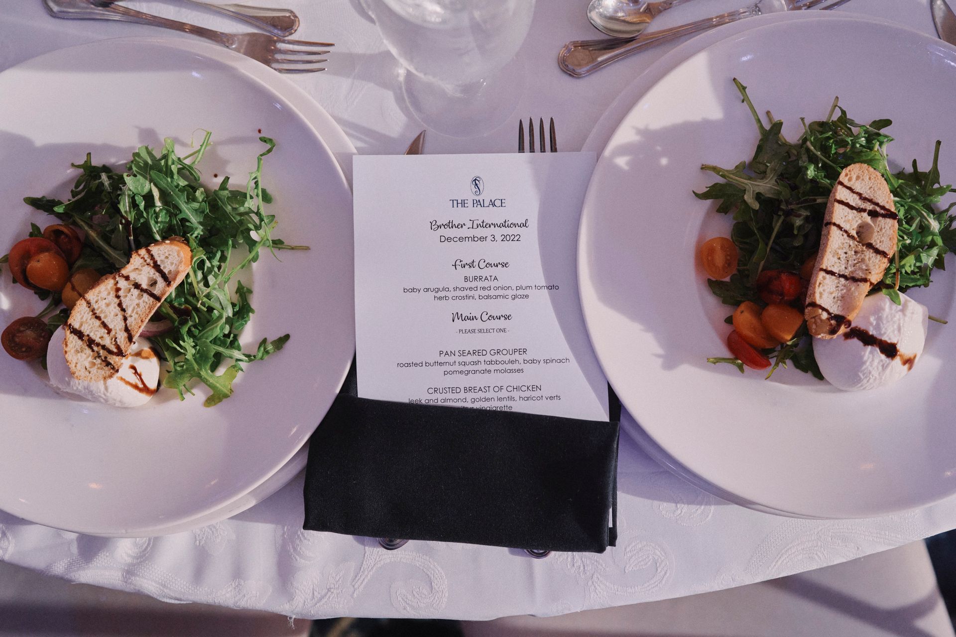 Two plates of salad with bread and menu card on a white tablecloth.