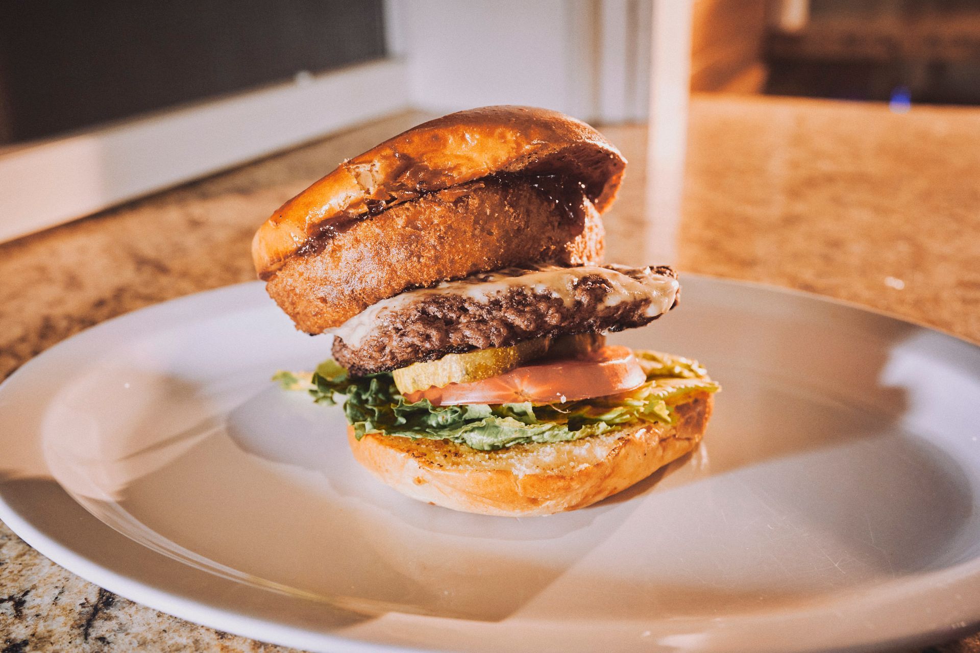 A close up of a hamburger on a white plate on a table.