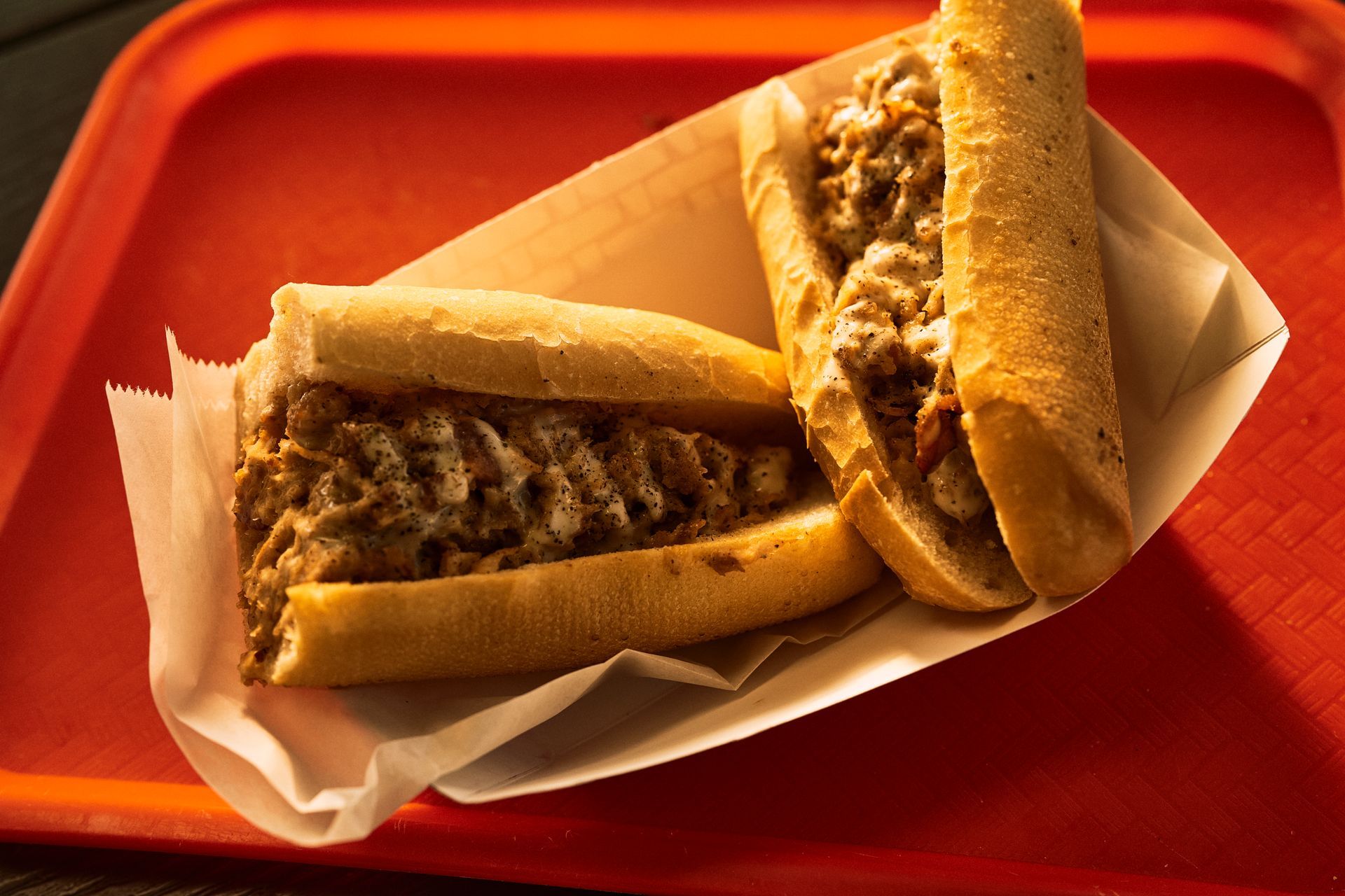 Two Philly cheesesteaks on a red tray, inside paper liners.