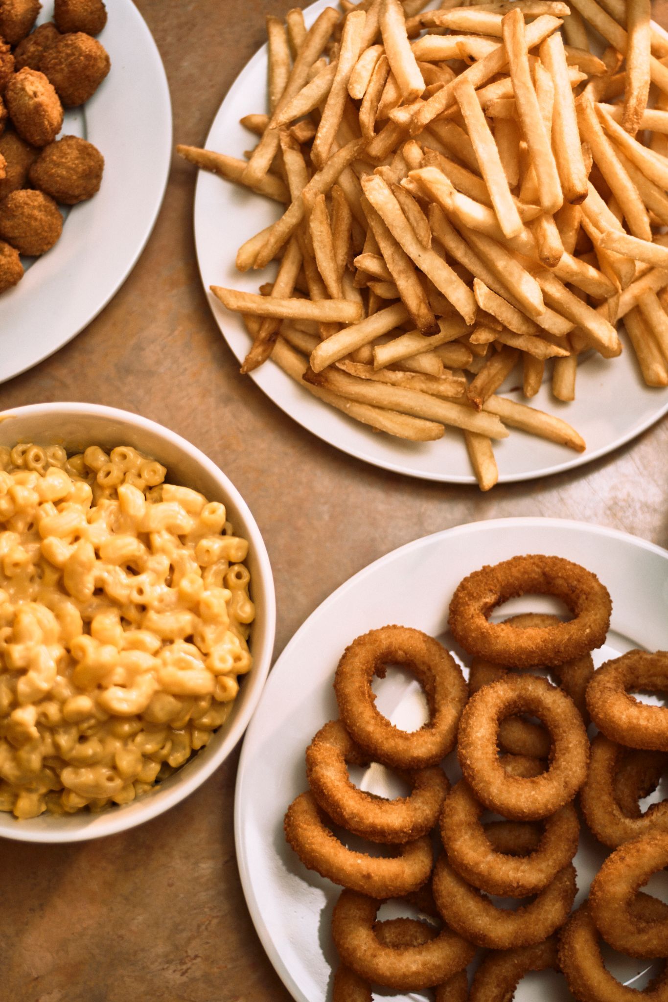 A table topped with plates of french fries , macaroni and cheese , and onion rings.
