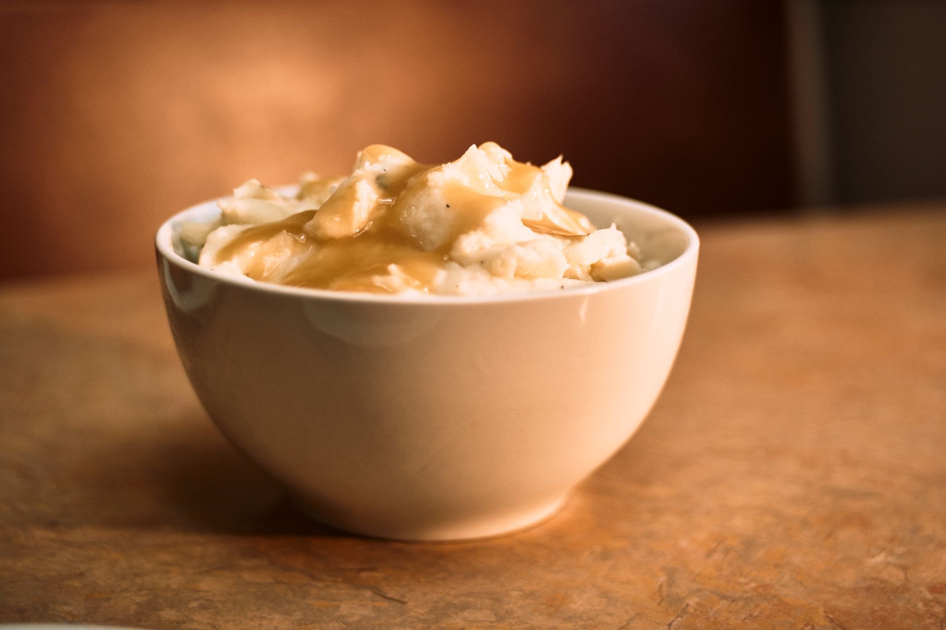 Bowl of mashed potatoes with gravy on a brown surface.