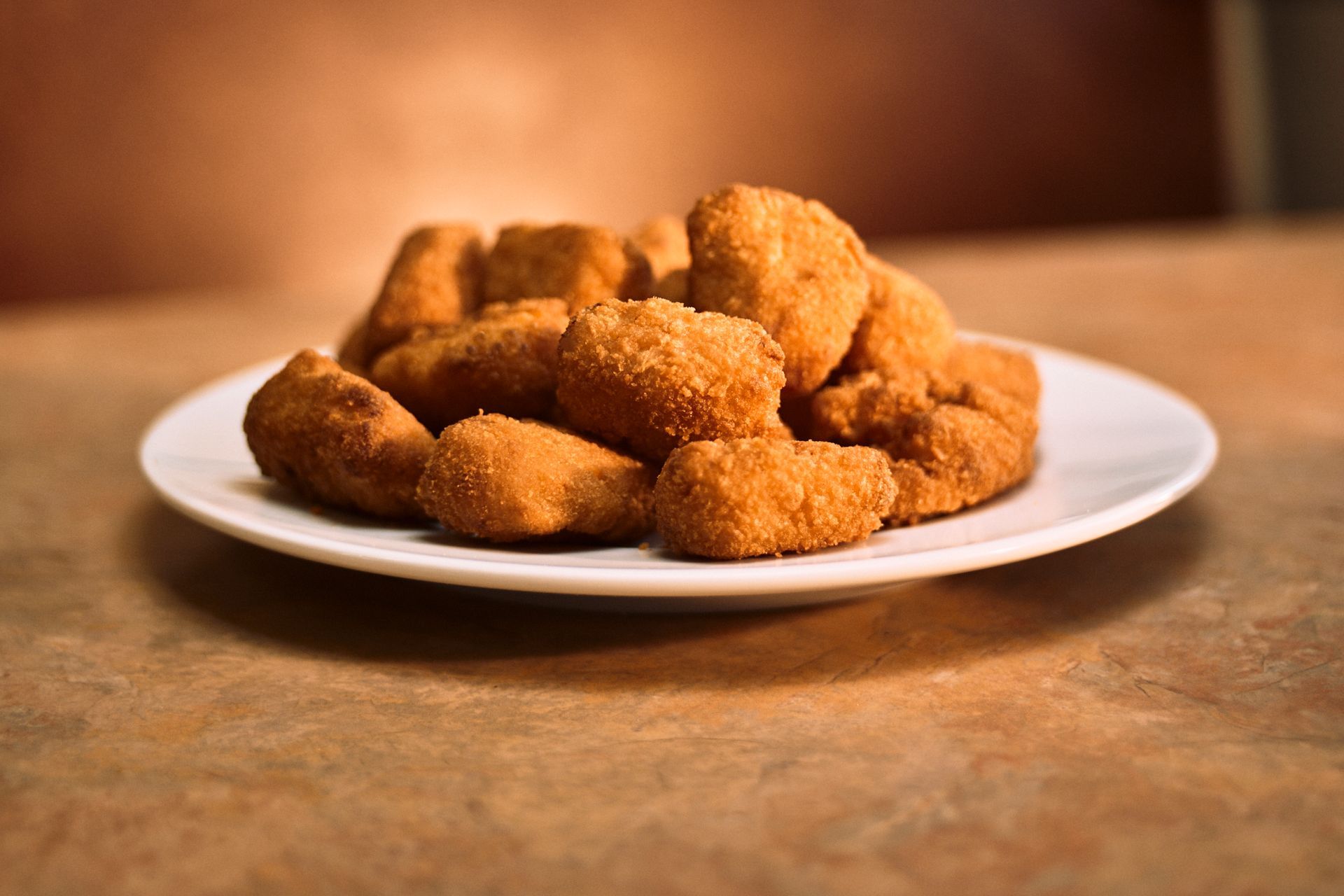 A white plate topped with fried chicken nuggets on a table.